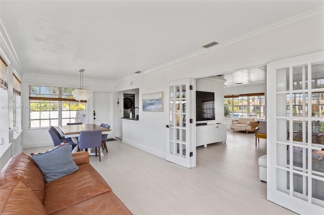 living room with stacked washing maching and dryer, wood-type flooring, a notable chandelier, and crown molding