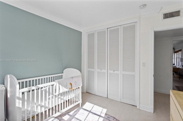 bedroom with a crib, crown molding, light wood-type flooring, and a closet