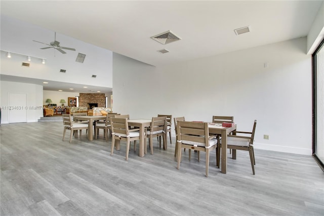 dining area featuring ceiling fan, rail lighting, a large fireplace, and light wood-type flooring