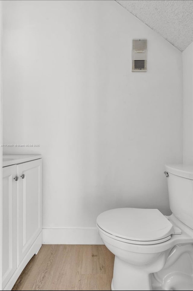 bathroom with wood-type flooring, toilet, vaulted ceiling, and a textured ceiling