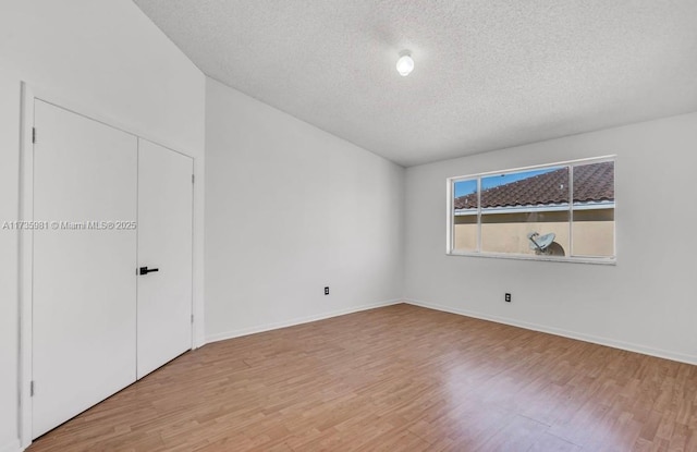 unfurnished bedroom featuring lofted ceiling, light hardwood / wood-style floors, and a textured ceiling