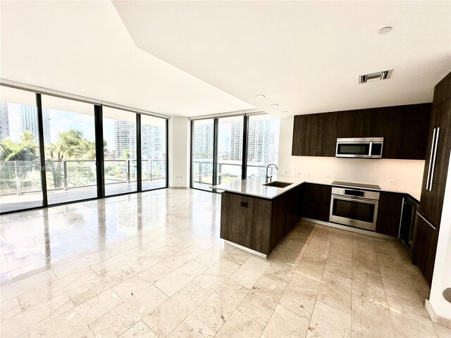 kitchen with sink, a wall of windows, appliances with stainless steel finishes, dark brown cabinetry, and kitchen peninsula