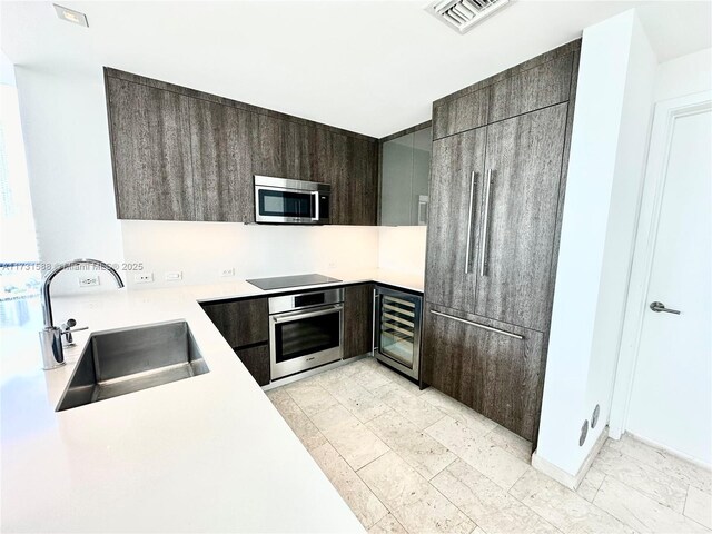 kitchen with stainless steel appliances, beverage cooler, sink, and dark brown cabinets