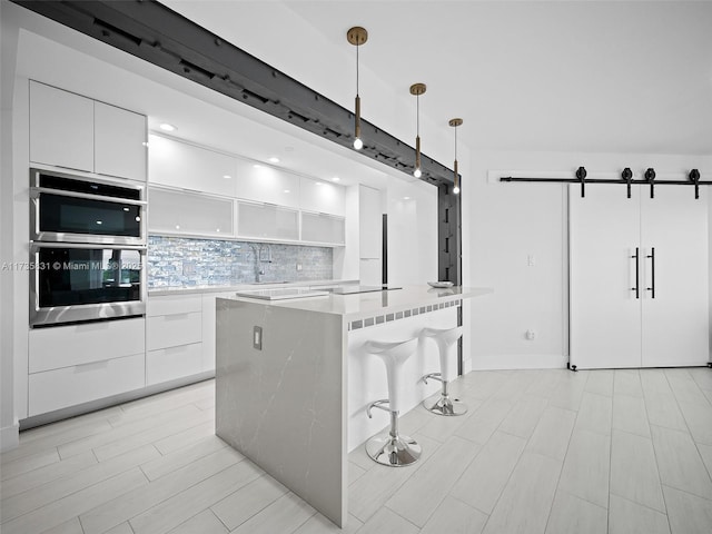 kitchen with decorative light fixtures, a center island, white cabinets, stainless steel double oven, and backsplash