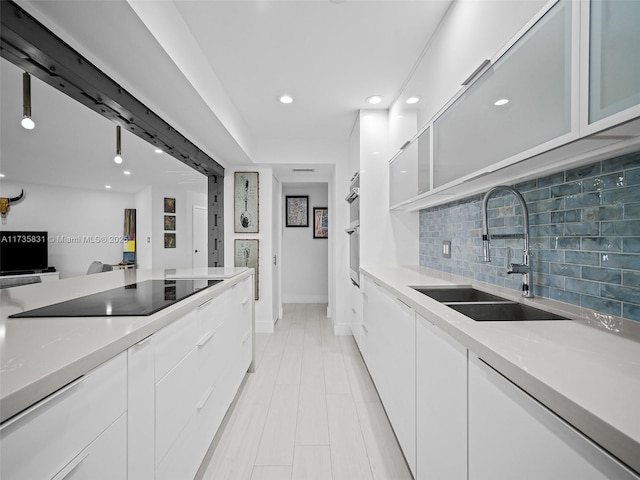 kitchen with light stone counters, black electric stovetop, sink, and white cabinets