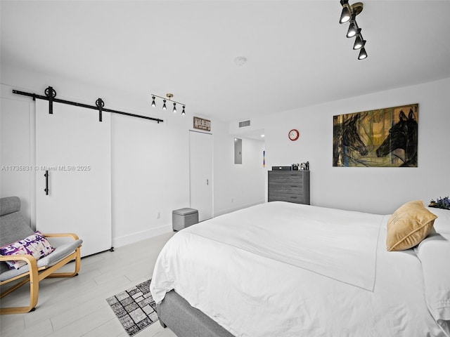 bedroom featuring a barn door, track lighting, electric panel, and light wood-type flooring