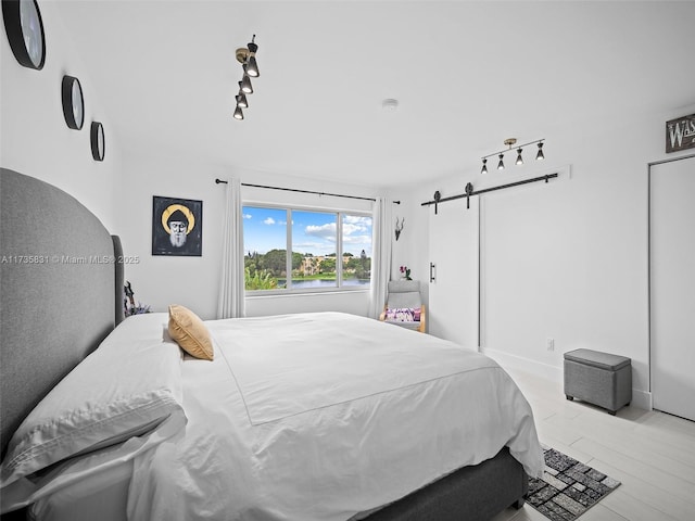 bedroom with rail lighting, a barn door, and light hardwood / wood-style flooring