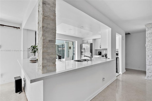 kitchen with stainless steel fridge, kitchen peninsula, sink, and white cabinets