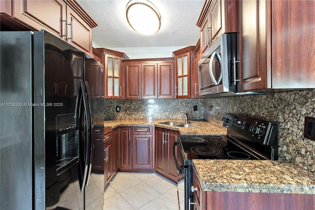 kitchen featuring sink, light tile patterned floors, backsplash, light stone counters, and black appliances