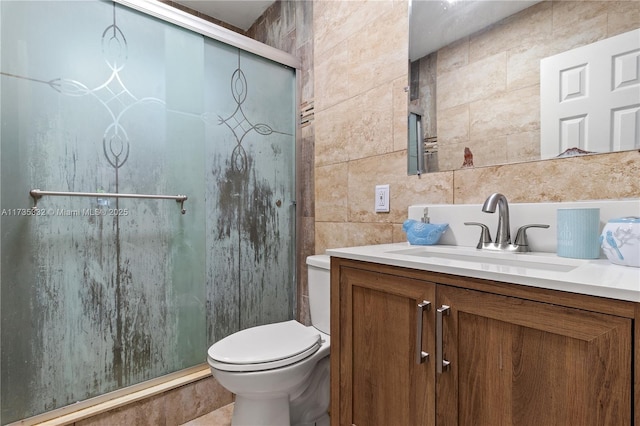 bathroom with vanity, toilet, a shower with shower door, and tile walls