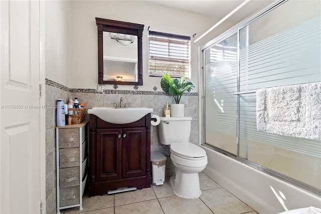 full bathroom with bath / shower combo with glass door, tile walls, vanity, toilet, and tile patterned floors