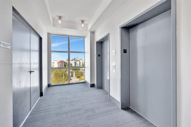 hallway with a tray ceiling, carpet floors, floor to ceiling windows, and elevator