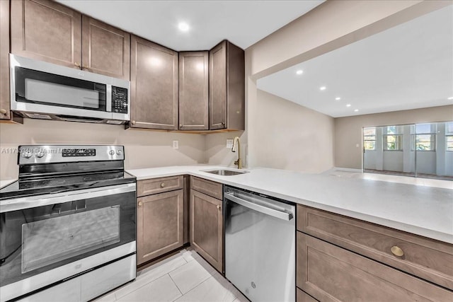 kitchen featuring appliances with stainless steel finishes, sink, light tile patterned floors, dark brown cabinetry, and kitchen peninsula