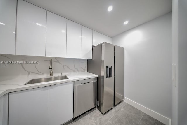 kitchen featuring sink, white cabinetry, stainless steel appliances, light stone counters, and decorative backsplash