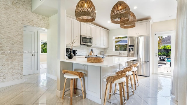 kitchen with a peninsula, light countertops, appliances with stainless steel finishes, a kitchen bar, and backsplash