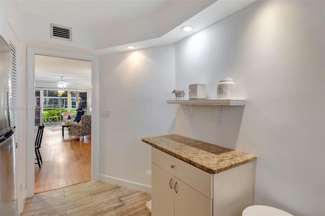 bar featuring light stone counters, light hardwood / wood-style floors, and ceiling fan