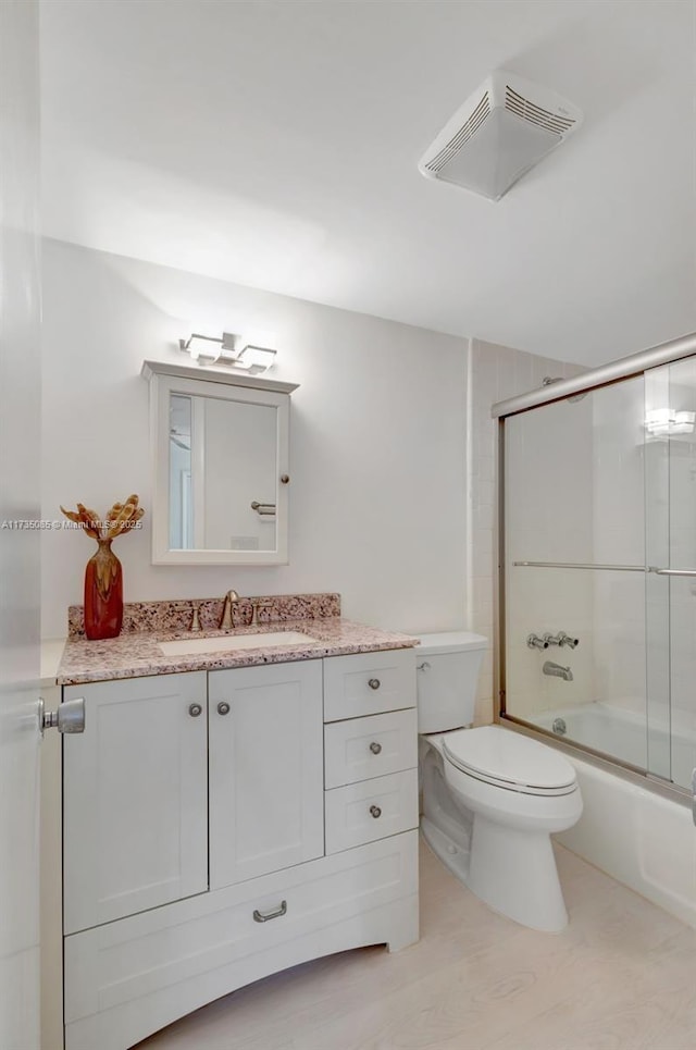 full bathroom featuring vanity, bath / shower combo with glass door, and toilet