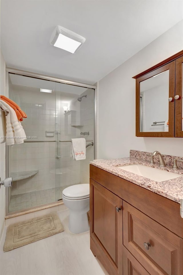 bathroom featuring vanity, toilet, and a shower with door