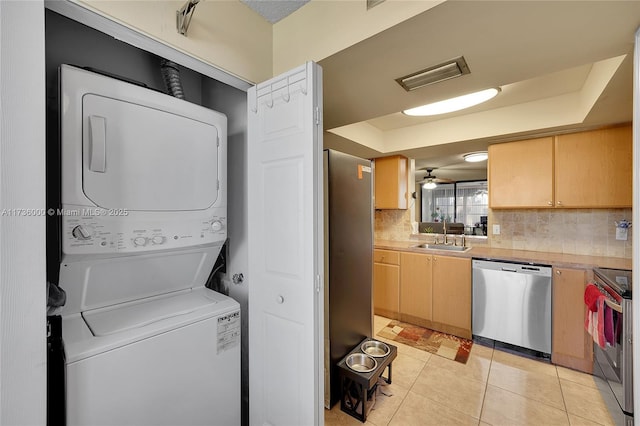 clothes washing area with ceiling fan, stacked washer / dryer, sink, and light tile patterned floors