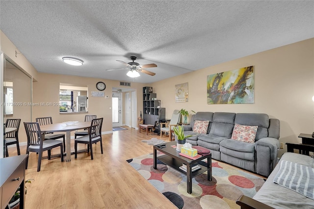 living room with a textured ceiling, ceiling fan, and light wood-type flooring