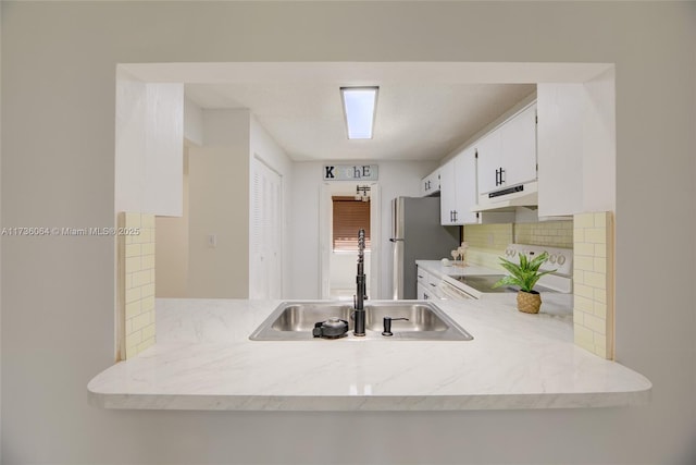 kitchen with sink, stainless steel refrigerator, stove, tasteful backsplash, and white cabinets