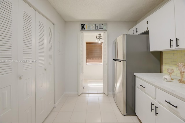 kitchen with light tile patterned flooring, a textured ceiling, stainless steel fridge, white cabinets, and backsplash