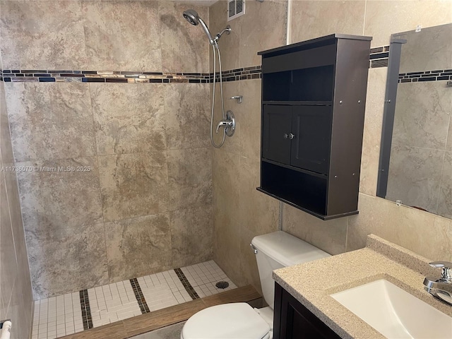 bathroom featuring a tile shower, vanity, tile walls, and toilet