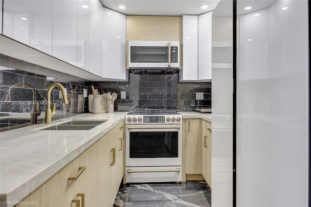 kitchen with sink, light stone counters, white cabinets, high end stove, and backsplash