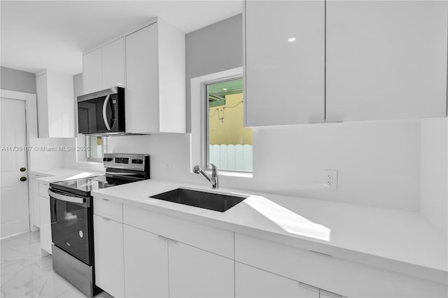 kitchen with appliances with stainless steel finishes, a wealth of natural light, sink, and white cabinets