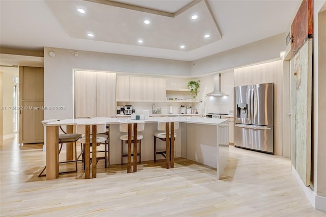 kitchen with a breakfast bar area, a center island, light hardwood / wood-style floors, stainless steel refrigerator with ice dispenser, and wall chimney exhaust hood