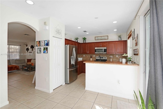 kitchen featuring arched walkways, light countertops, appliances with stainless steel finishes, light tile patterned flooring, and a peninsula