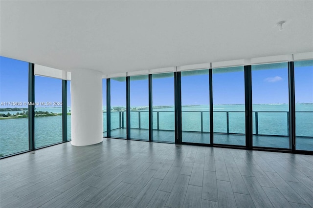 unfurnished room featuring floor to ceiling windows, a water view, and wood-type flooring