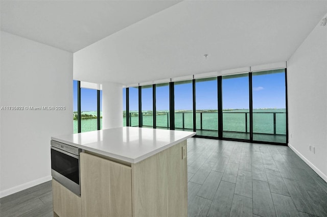 kitchen featuring floor to ceiling windows, a water view, a center island, light brown cabinets, and dark hardwood / wood-style floors