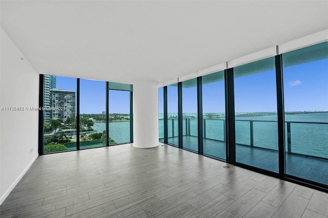 unfurnished room with floor to ceiling windows, a water view, and light hardwood / wood-style floors