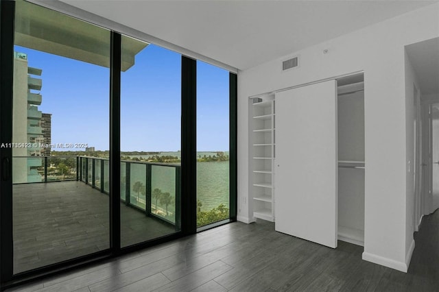 unfurnished bedroom featuring expansive windows, a water view, and dark hardwood / wood-style floors