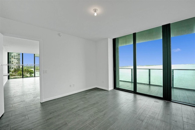 empty room featuring a water view, hardwood / wood-style floors, and a wall of windows