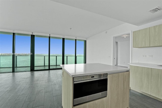 kitchen with a wall of windows, a center island, a water view, wood-type flooring, and oven