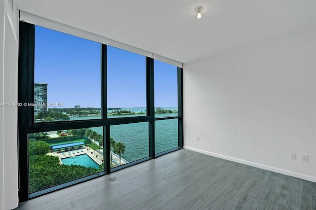 empty room featuring expansive windows, a water view, and hardwood / wood-style floors