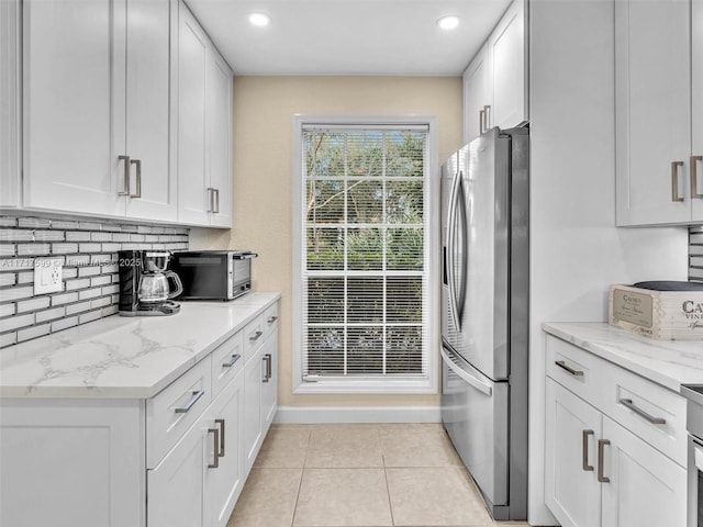 kitchen with light stone counters, light tile patterned floors, stainless steel fridge, decorative backsplash, and white cabinets