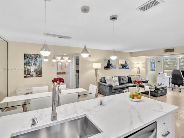 kitchen with stainless steel dishwasher, decorative light fixtures, light stone countertops, and sink