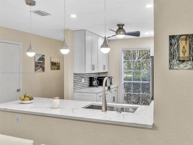 kitchen featuring sink, backsplash, light stone counters, decorative light fixtures, and kitchen peninsula