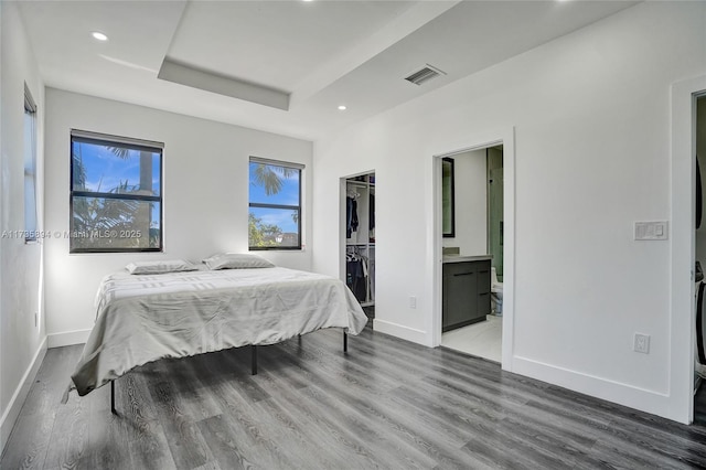 bedroom featuring hardwood / wood-style flooring, ensuite bathroom, a raised ceiling, a walk in closet, and a closet