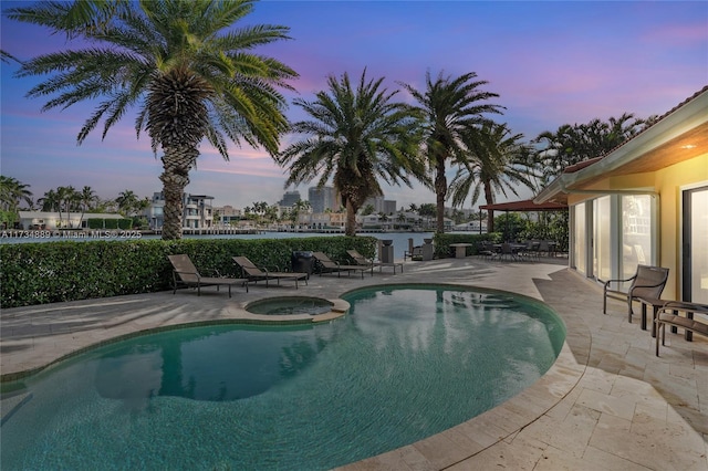 pool at dusk with a patio and an in ground hot tub