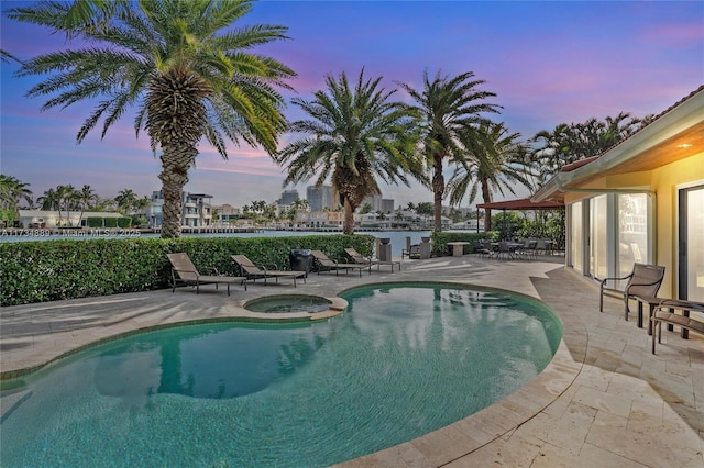 pool at dusk featuring a pool with connected hot tub and a patio area