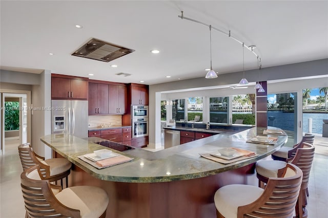 kitchen featuring a water view, appliances with stainless steel finishes, a kitchen breakfast bar, pendant lighting, and backsplash