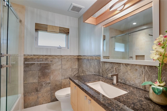 full bathroom featuring vanity, enclosed tub / shower combo, tile walls, and toilet