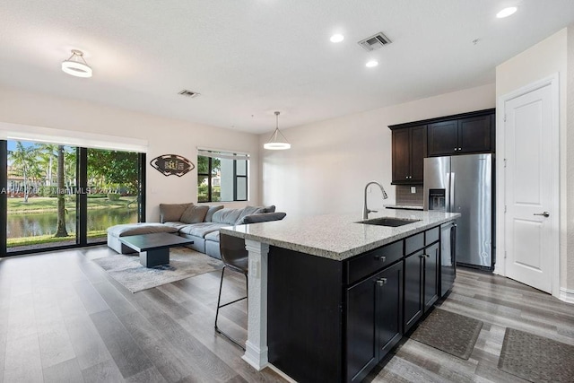 kitchen featuring sink, appliances with stainless steel finishes, a kitchen island with sink, light stone counters, and wood-type flooring