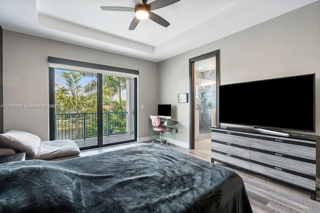 bedroom with a tray ceiling, access to exterior, connected bathroom, and light hardwood / wood-style floors