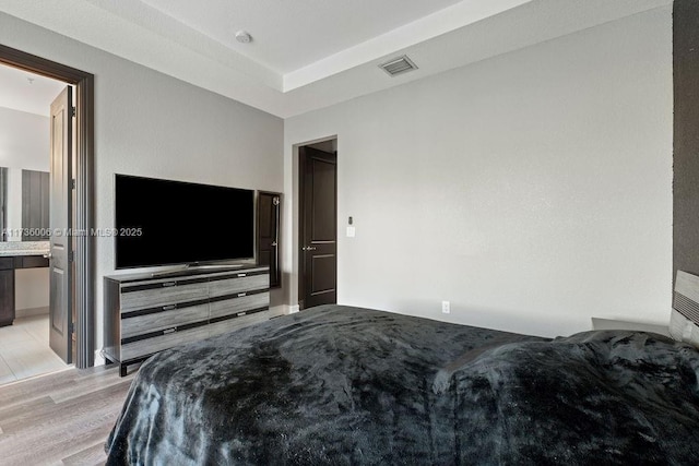 bedroom featuring connected bathroom, a raised ceiling, and light wood-type flooring