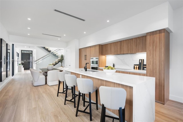 kitchen featuring tasteful backsplash, stainless steel double oven, a breakfast bar area, and a large island with sink